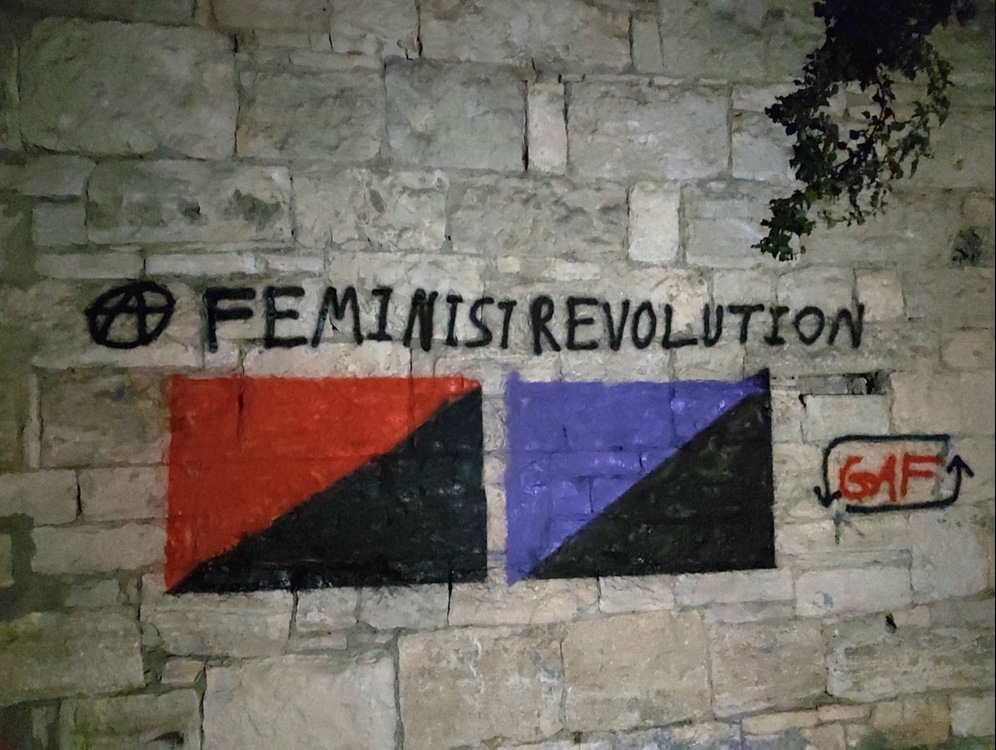 Graffiti showing a Anarcho-Communist and an Anarcha-Feminist Flag with the writing "Feminist Revolution" alongside an Anarchist A